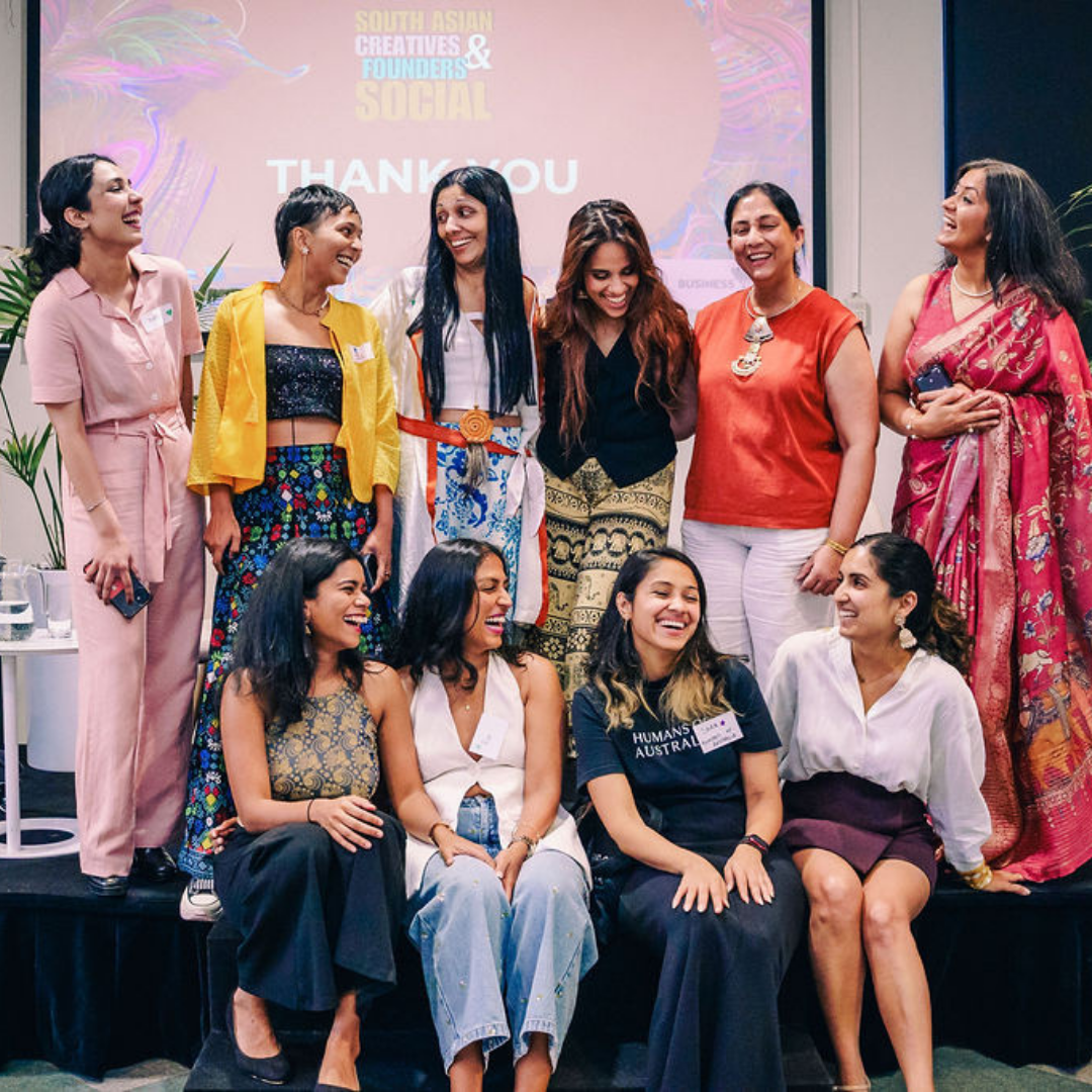 A group of South Asian women creatives and founders laughing together on stage at a community event.